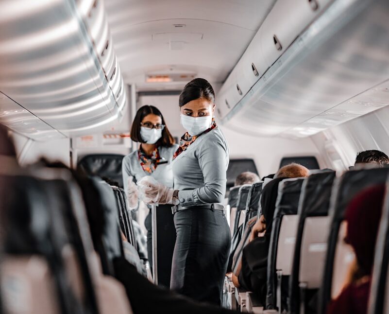 air hostess wearing a facemask standing in the aisle of an aeroplane